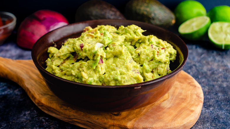 Guacamole in bowl with lime and avocado in background