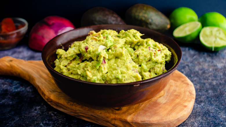 Guacamole in a bowl surrounded by fruits and vegetables