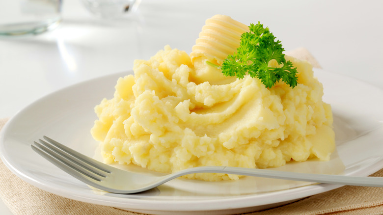 Mashed potatoes topped with butter and garnish on a plate with a fork