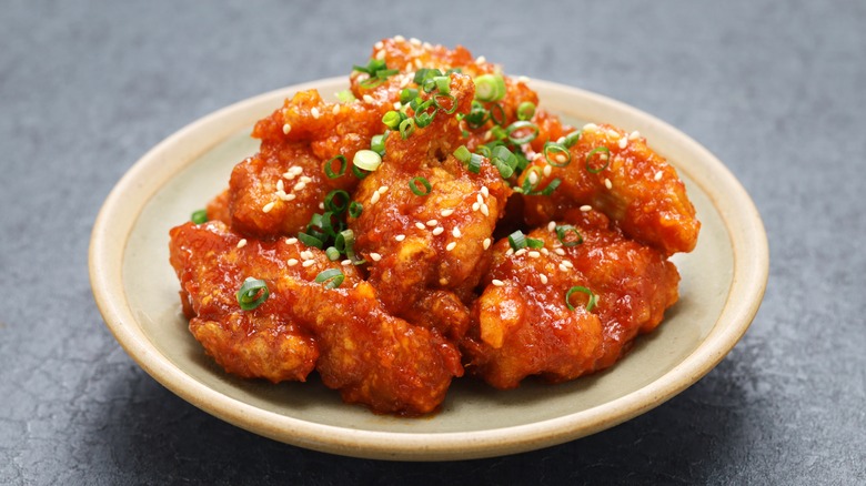 Korean style fried chicken wings on a plate topped with chopped scallions and sesame seeds
