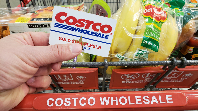 Costco card held in front of a cart full of food
