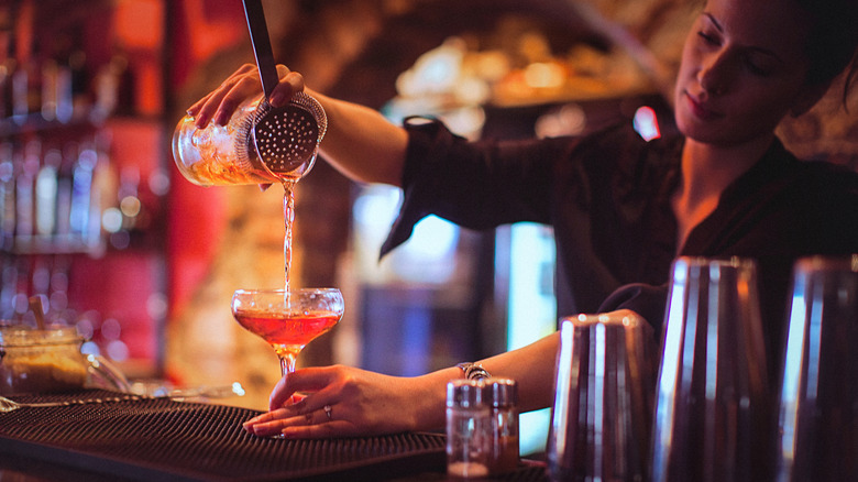 A bartender strains a cocktail into a glass