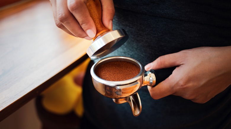 Hands tamping down coffee grounds