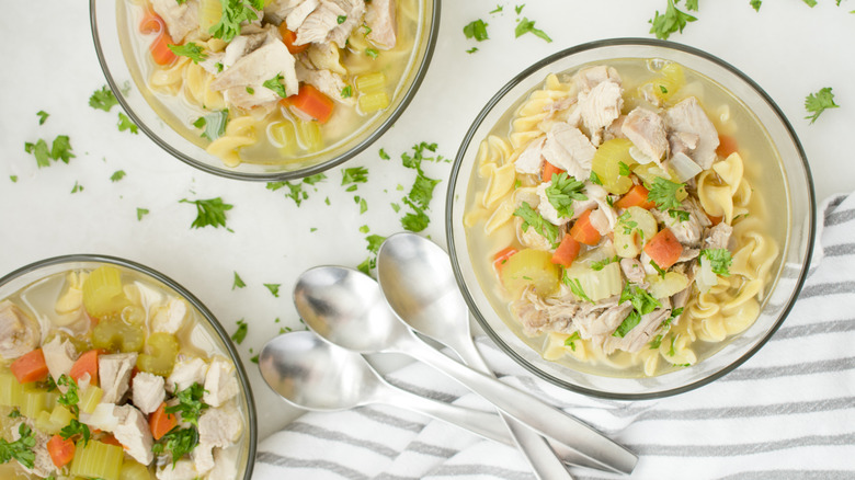 Three bowls of chicken soup with spoons