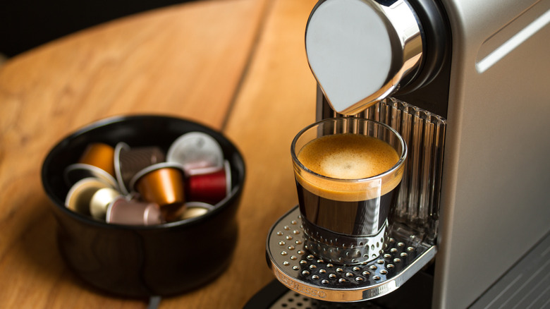 A Nespresso machine pouring a shot next to a bowl of Nespresso capsules