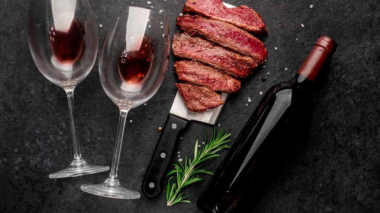 red wine glass next to sliced steak and wine bottle