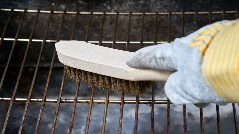 gloved hand cleaning grill with wooden brush