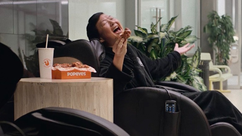 Ken Jeong in a massage chair eating Popeyes 