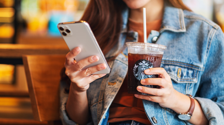 person holding a Starbucks coffee while looking at a smartphone