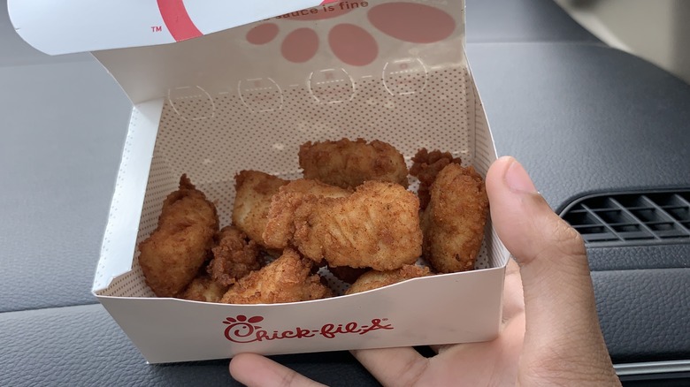 person holding a box of chick-fil-a nuggets in a car