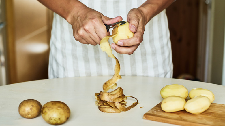 Person peeling potatoes with a potato peeler