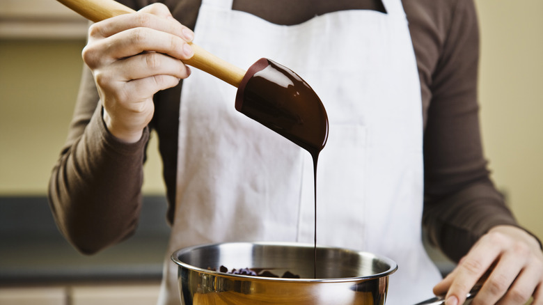Person dipping a spatula in a bowl of melted chocolate