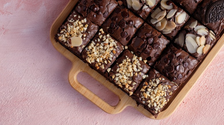 A tray of brownies topped with peanuts, chocolate chips, sliced almonds and oreos