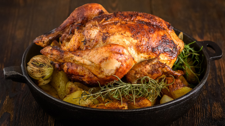 whole roasted chicken over vegetables in cast-iron pan