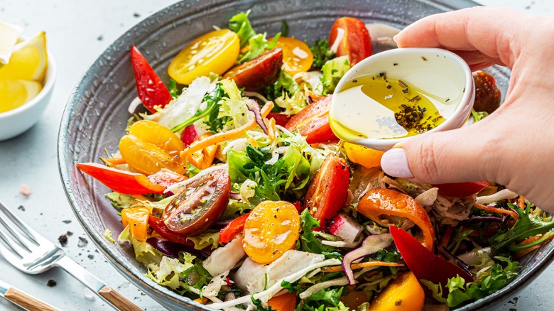 Person pouring dressing atop salad