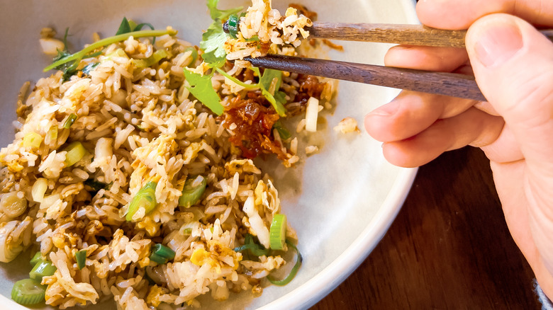 Fried rice in a dish with a hand holding chopsticks