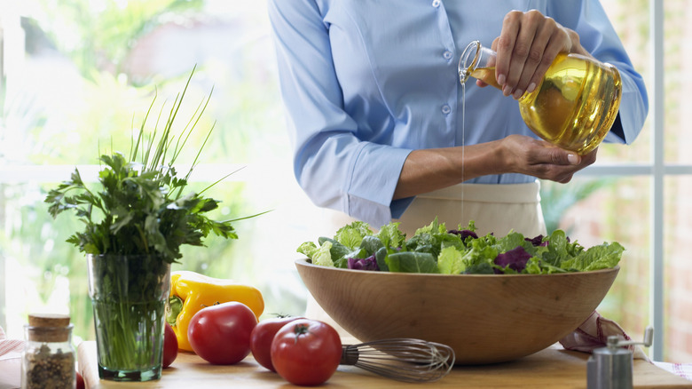 woman pouring oil over bowl of salad greens