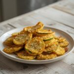 A plate of golden, crunchy zucchini chips seasoned with parmesan and garlic, ready to eat.