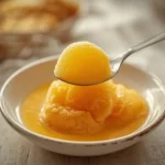 mango sorbet recipe: : Creamy homemade mango sorbet in a white bowl with a spoon.