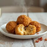 A plate of golden brown loaded mashed potato balls, crispy and ready to eat, with visible bits of cheese and bacon.