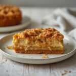 Apple crumble cheesecake with biscoff crust, spiced cheesecake layer, cinnamon apples, and buttery crumble topping served on a table.