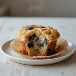 Freshly baked bakery style blueberry muffins with golden tops on a baking sheet, showcasing juicy blueberries.