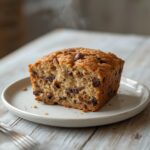 A golden brown chocolate chip banana bread loaf with visible chocolate chips on a rustic table.