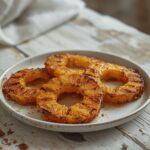 A plated grilled pineapple with caramelized brown sugar, topped with a scoop of vanilla ice cream on a table.