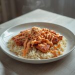 A complete Korean spicy pork bowl with marinated pork, rice, noodles, and drizzled sauces on a table.