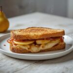 A golden grilled cheese sandwich filled with pear, apple, and caramelized onions served on a plate.