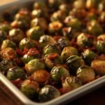 A full sheet pan of roasted Brussels sprouts with bacon and a drizzle of balsamic glaze.