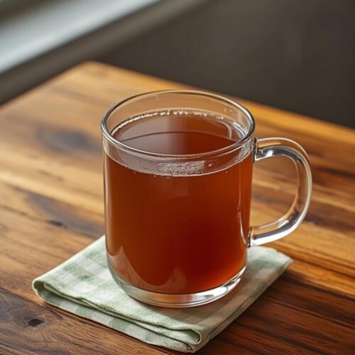 A glass mug filled with nutritious homemade bone broth recipe on a rustic wooden table.