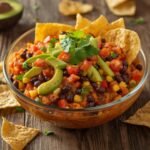 A colorful glass bowl of chunky cowboy caviar served with a crisp tortilla chip.