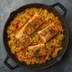 A delicious and colorful one pot salmon and rice served in a black cooking skillet.